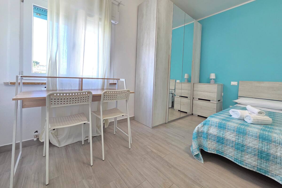 Un dormitorio con cama, escritorio, sillas, armario y espejo.