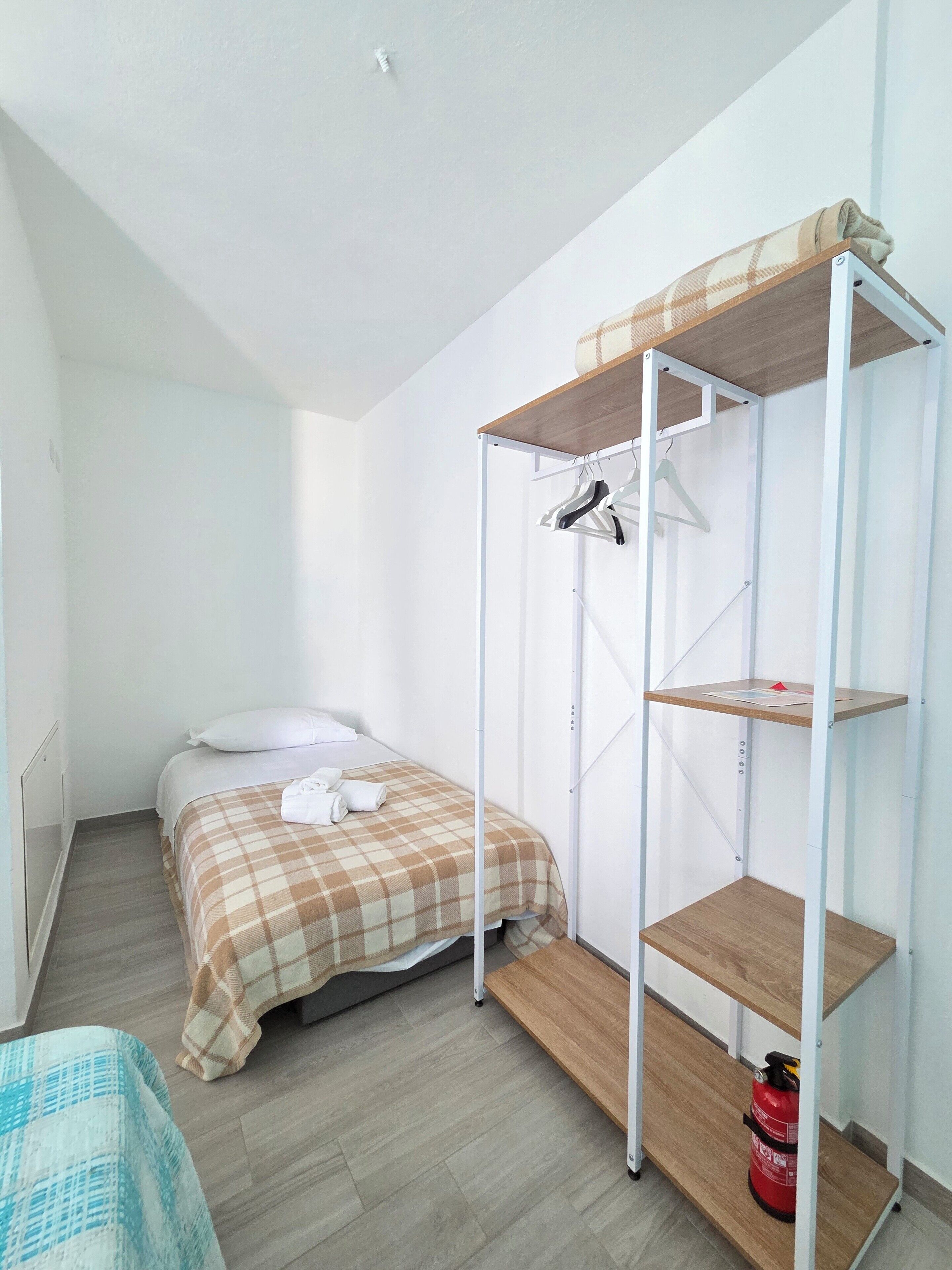 Een kleine eenpersoonskamer met een stapelbed, een houten plank en een brandblusser.