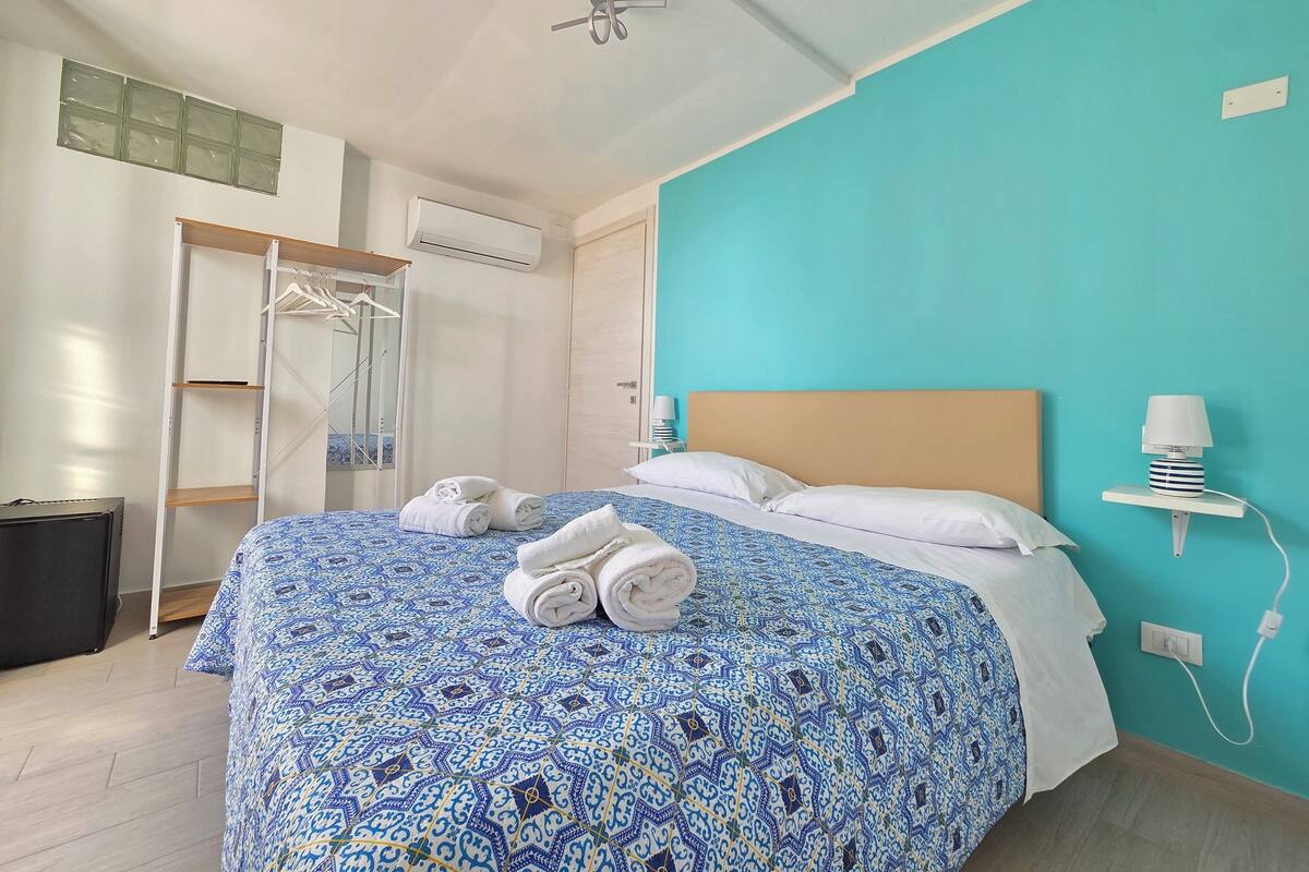 Habitación de hotel con cama, armario, perchero y mesita de noche con lámpara.