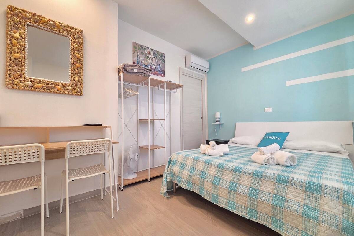 Una habitación de hotel con cama, escritorio, silla, armario y espejo.