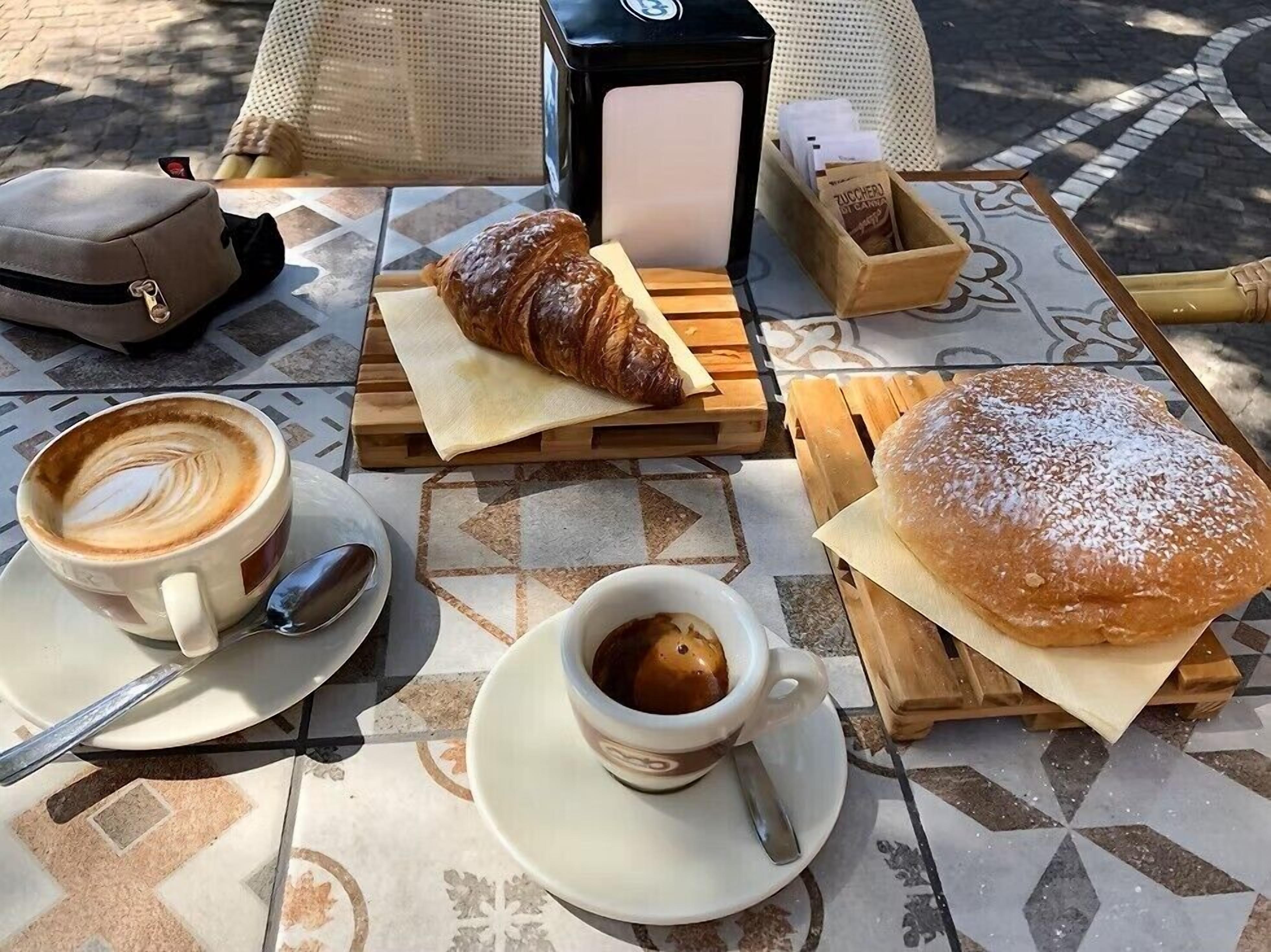 Una mesa con un croissant, un pastel, una taza de café y una cesta de pasteles.