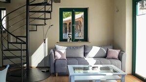 Un salón moderno con un sofá gris, una mesa de centro de vidrio, una escalera espiral y un ventanal con vista a un edificio.