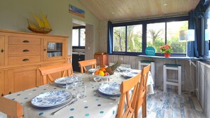 Uma sala de jantar com uma mesa posta para quatro pessoas, cadeiras de madeira, um armário de madeira e uma janela com vista para árvores.