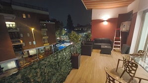 Terraço no telhado com área de estar, piscina e vista para a cidade à noite.