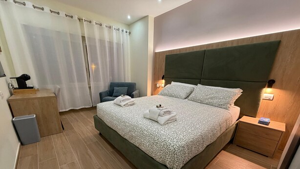 Quarto moderno com uma cama grande, mesa de cabeceira, cadeira, escrivaninha e lixeira.