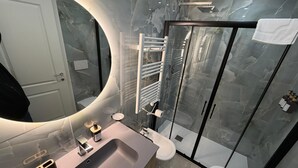 Uma casa de banho moderna com lavatório de mármore, um espelho grande, cabine de duche e sanita.