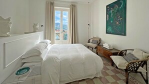 Hotelkamer met een bed, een stoel, een bureau, een schilderij en uitzicht op gebouwen door het raam.