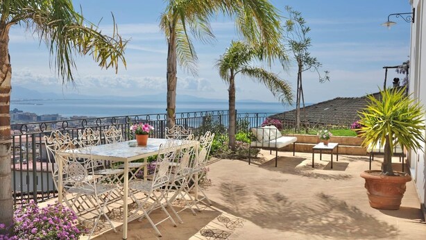 A terrace with a table and chairs, a potted plant, and a view of the sea. - Villa Ipomea - Cielo & Terra (Salerno)
