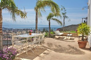 Eine Terrasse mit Tisch und Stühlen, einem Blumentopf und Blick aufs Meer.