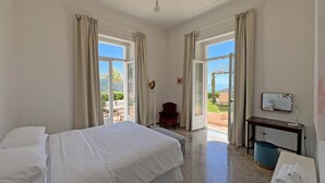 A hotel room with a bed, a desk with a lamp, a chair, and a view of the outdoors. - Villa Ipomea - Cielo & Terra (Salerno)