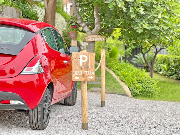 Ein rotes Hybridauto parkte neben einem Holzschild mit einem Parkplatzsymbol und dem Text 'CIELO TERRA', das nach rechts weist.