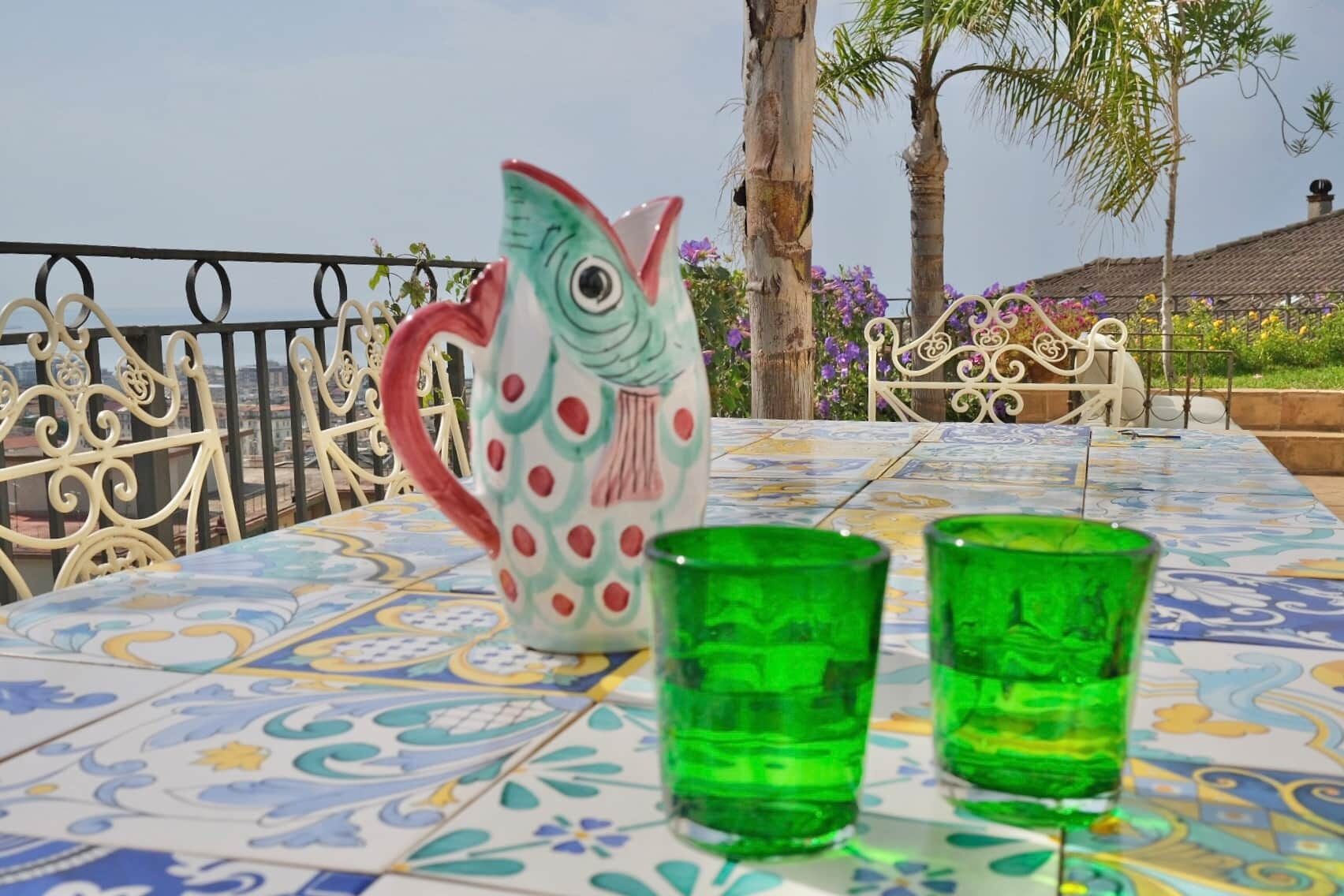 Una mesa con un mantel colorido, una jarra con forma de pez y dos vasos verdes.