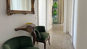 Een gang met een spiegel, een console tafel, twee groene stoelen en een deur die leidt naar een andere kamer met groene vazen op een plank.