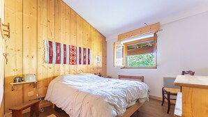 Ein Zimmer mit Holzboden, einem Bett, einem Schreibtisch, einem Stuhl und einem Fenster.