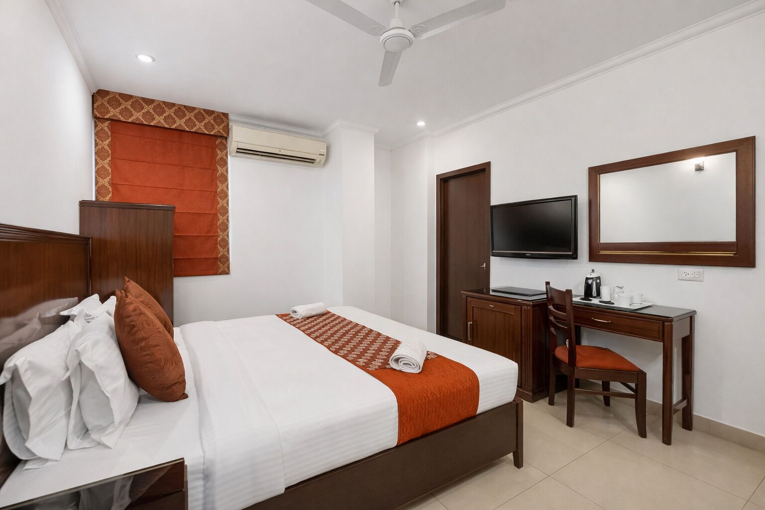 A hotel room with a bed, a desk, a chair, a television, and an air conditioning unit.