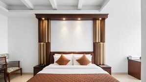 Una habitación de hotel con una cama grande, cabecera de madera, dos mesitas de noche, una silla y un buró con un teléfono.
