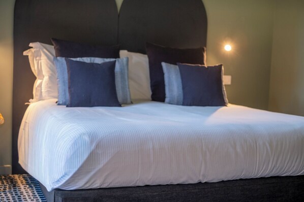 A neatly made bed with white linens and dark pillows, a dark headboard, and a small bedside lamp. - HT Vatican cozy rooms & apartments (Rome)