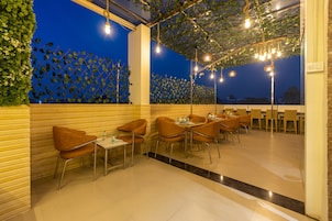 An outdoor dining area with tables and chairs, a leafy wall, and string lights.
