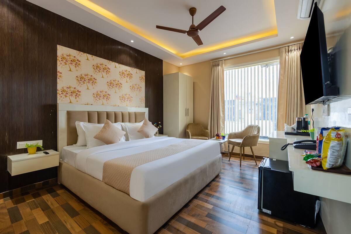 A hotel room with a large bed, a desk, a chair, a ceiling fan, and a window with curtains.