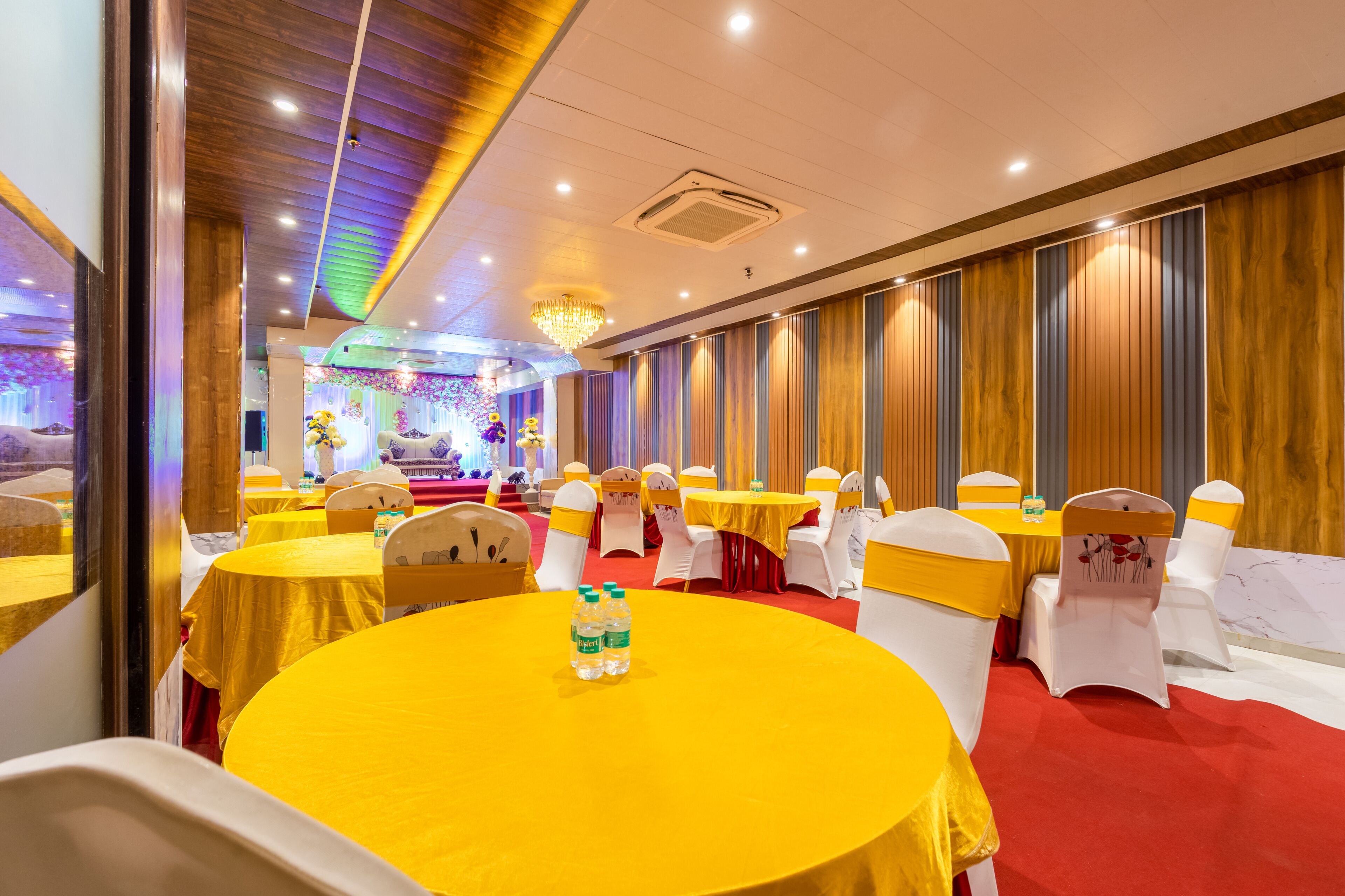 A banquet hall with round tables, white chairs, and yellow tablecloths.