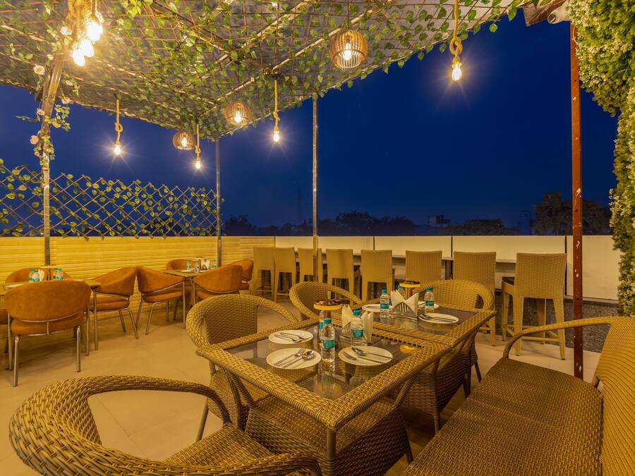 Un área de comedor al aire libre con muebles de mimbre e iluminación colgante, frente a un cielo nocturno.