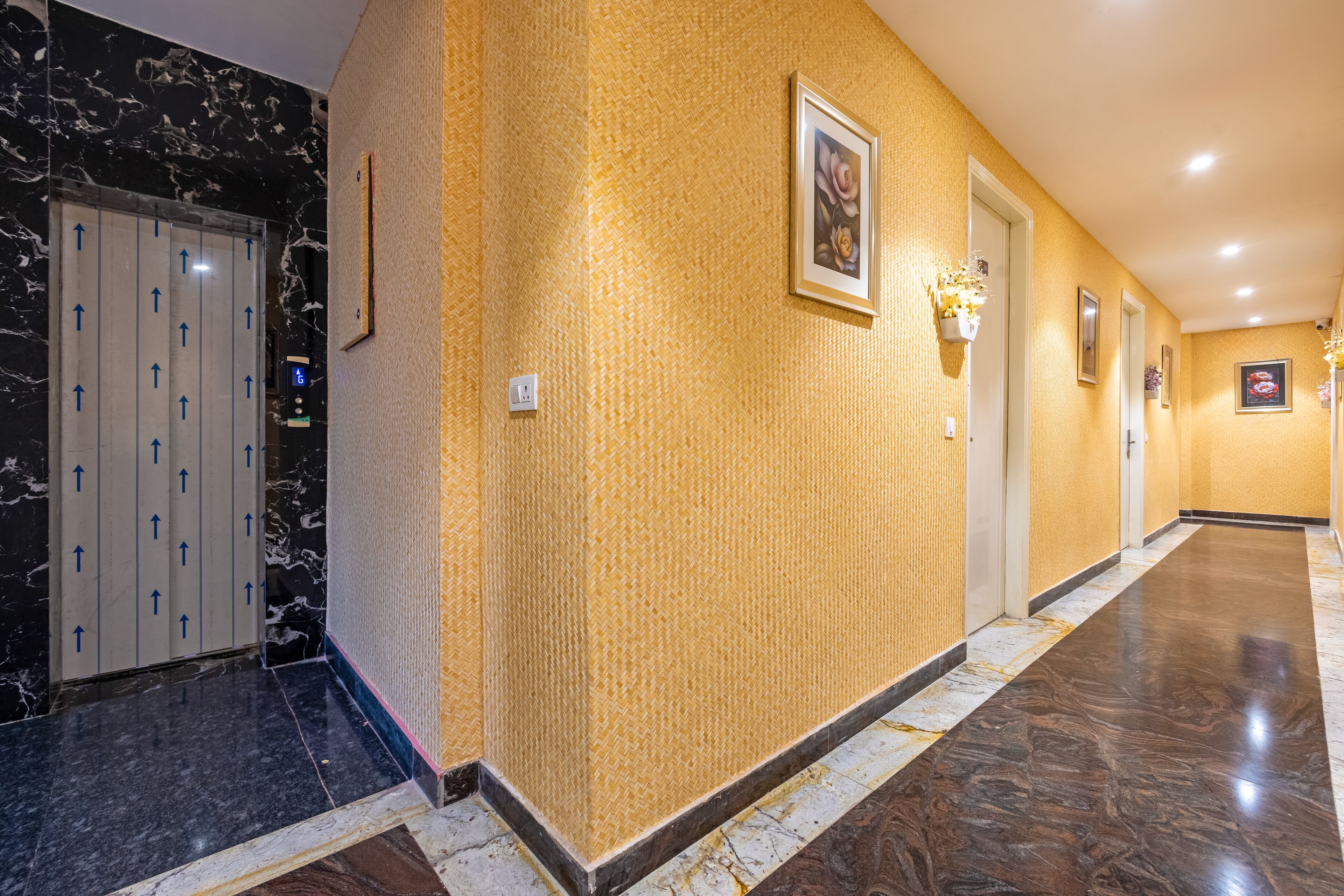 A hotel hallway with marble flooring, a textured yellow wall, and a door with arrows indicating direction.