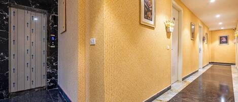 A hotel hallway with marble flooring, a textured yellow wall, and a door with arrows indicating direction.
