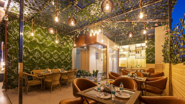 Ein Restaurant mit Korbmöbeln, hängenden Lampen und einer begrünten Wand.