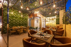 Ein Restaurant mit Korbmöbeln, hängenden Lampen und einer begrünten Wand.