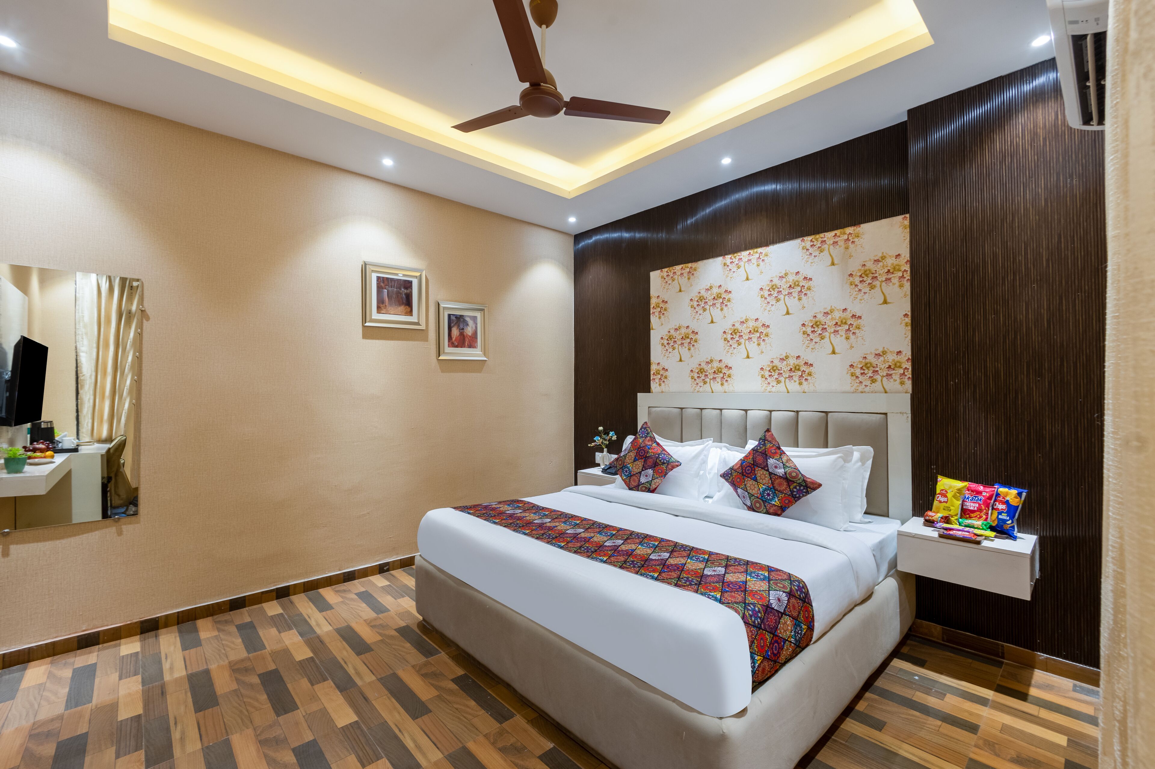 Une chambre d’hôtel moderne dotée d’un grand lit, d’un ventilateur de plafond, d’une table de chevet avec des en-cas et d’un climatiseur fixé au mur.