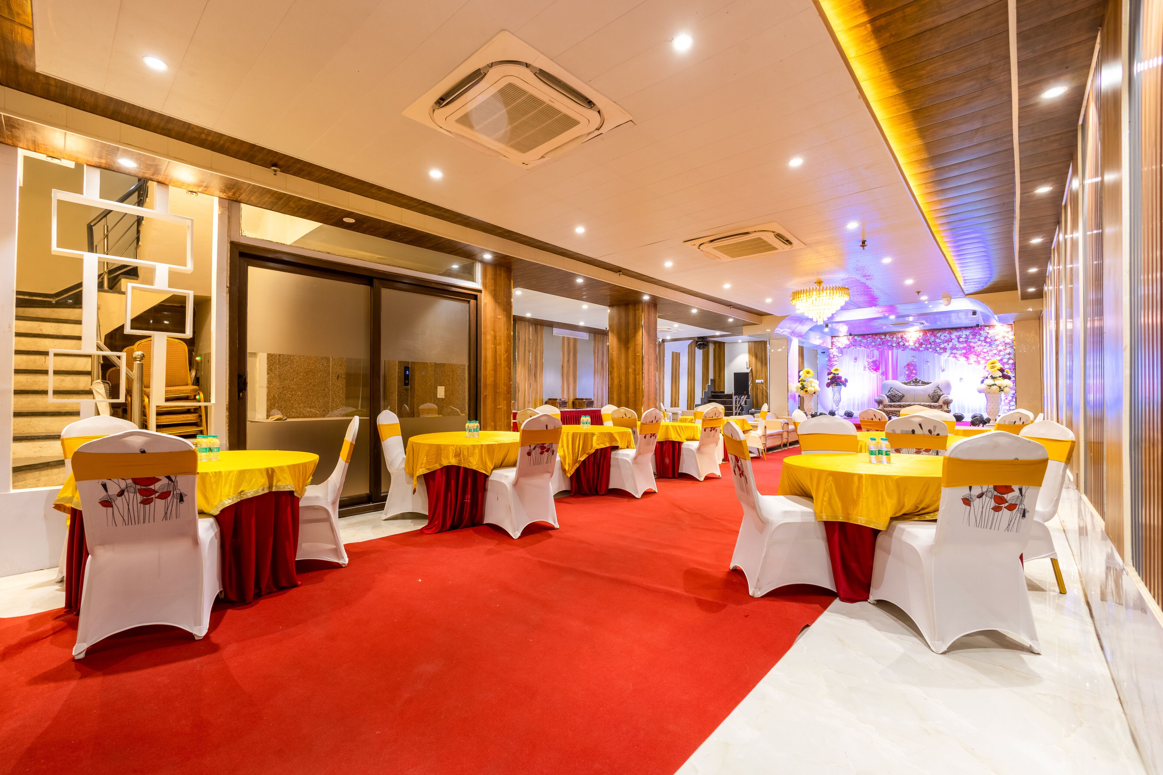 A banquet hall with round tables, white chairs, and red carpets.