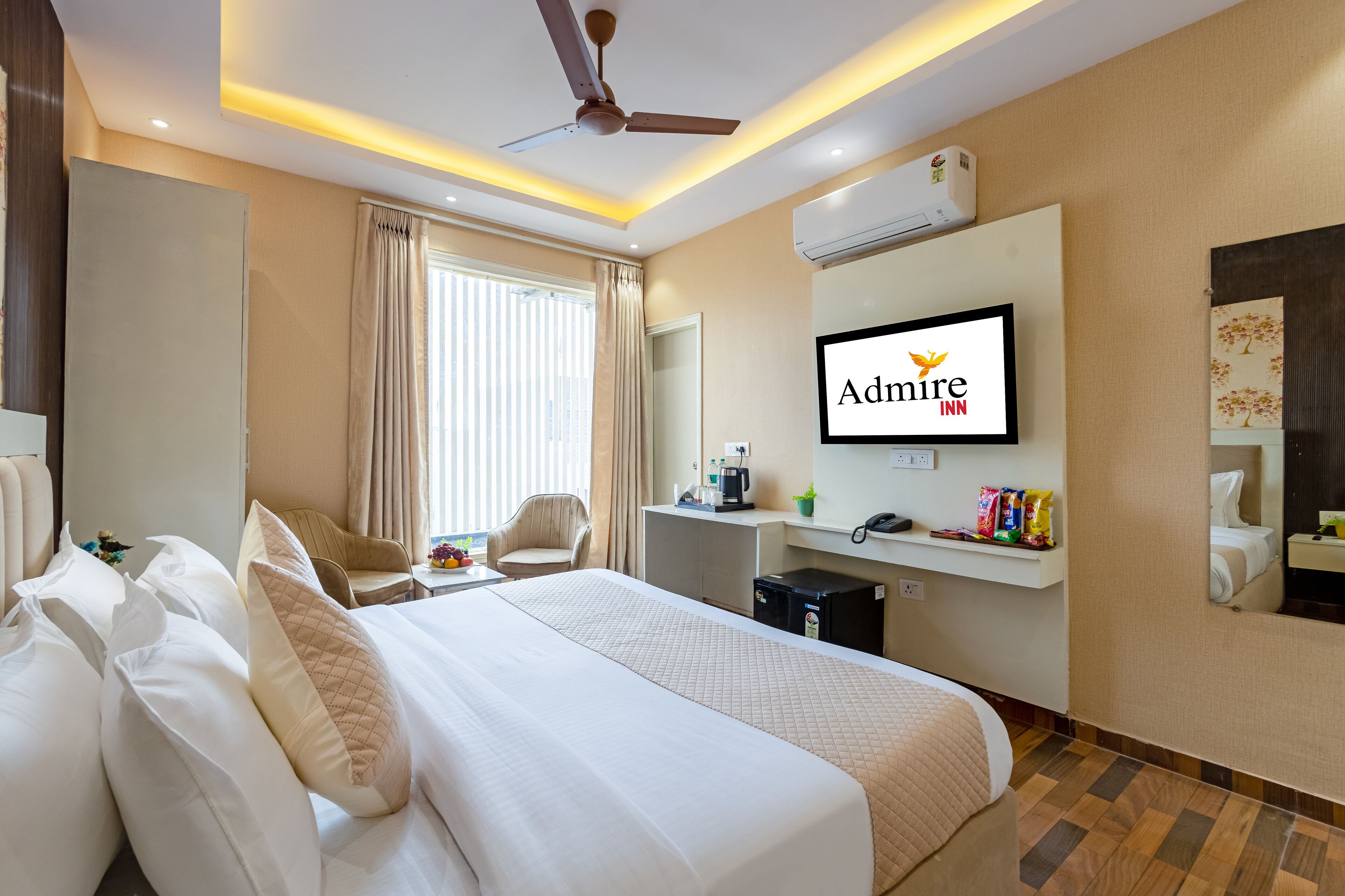 Una habitación de hotel con cama, escritorio, silla, televisor y espejo.