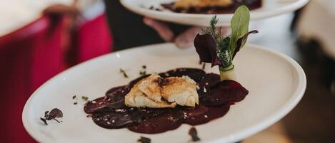 Un plato con un trozo de pescado, salsa oscura y verduras verdes.