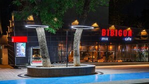 En moderne bygning med et skilt, der viser 'RIBICON mix cafe', omgivet af et cirkulært vandbassin med to træer.