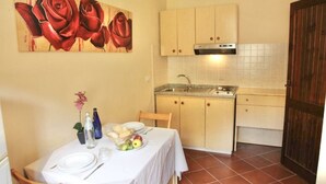 Une cuisine compacte avec un coin repas, comprenant une table mise avec des assiettes, des verres et un panier de fruits.