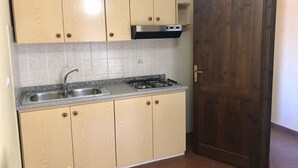 Une cuisine avec des meubles de couleur bois clair, un évier en acier inoxydable et une cuisinière à gaz.
