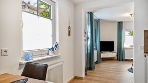 Ein modernes Wohnzimmer mit Fernseher, Holzboden und Blick durch ein Fenster.