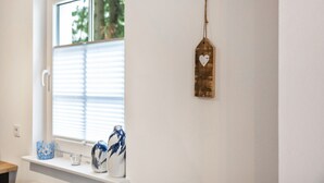 Ein Fenster mit Jalousien, eine Vase und ein an der Wand befestigtes dekoratives Schild.