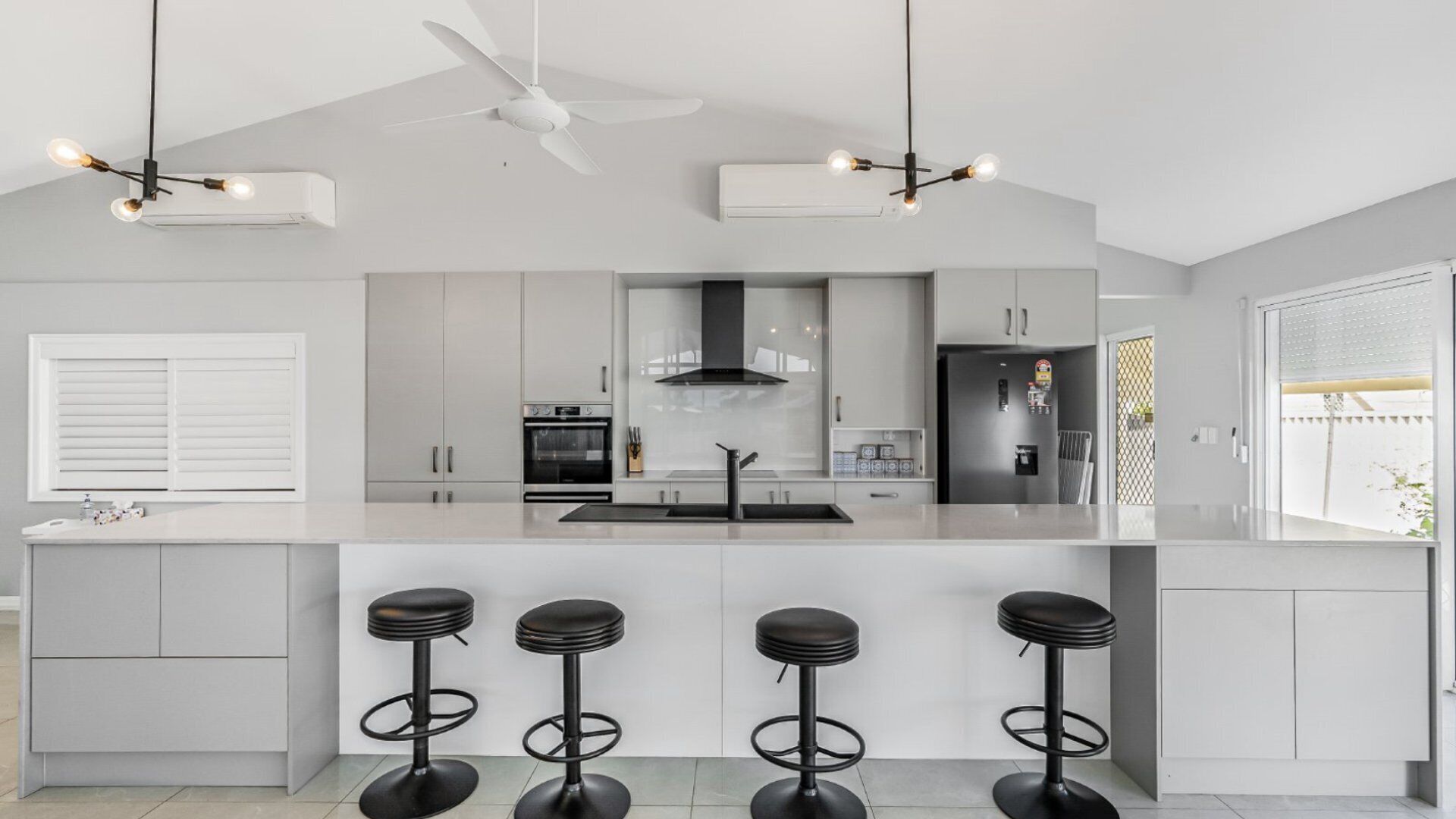 Een moderne keuken met een centraal eiland, barkrukken, een plafondventilator en een koelkast.