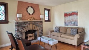 A living room with a stone fireplace, a sofa, a coffee table, and a painting on the wall. - Charming 3BR STL Home • Sleeps 6 • Free Parking (St. Louis)
