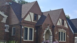 A brick house with a gabled roof, stone archway entrance, and a well-maintained garden. - Charming 3BR STL Home • Sleeps 6 • Free Parking (St. Louis)