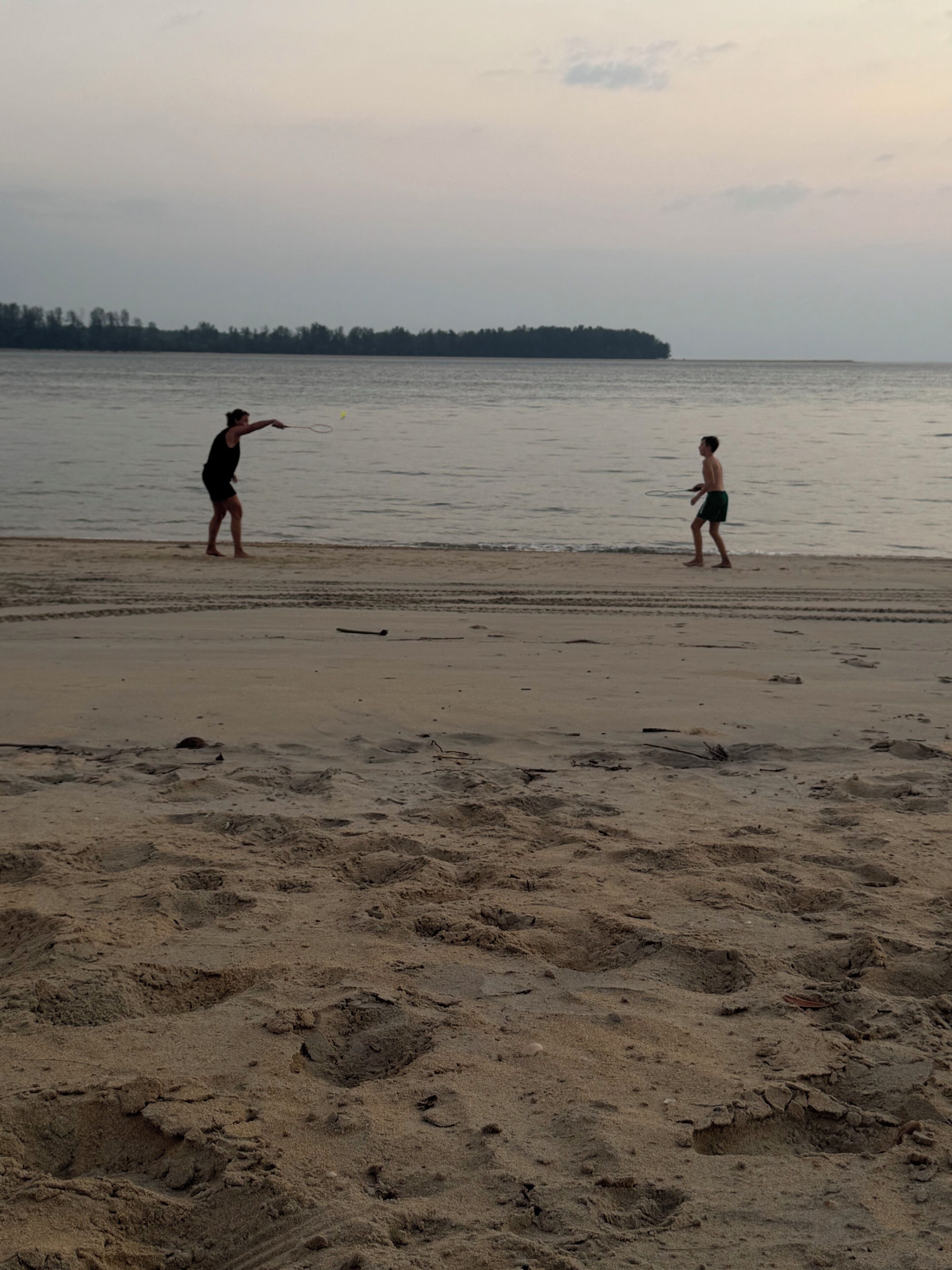 A beach with two people playing near the water.