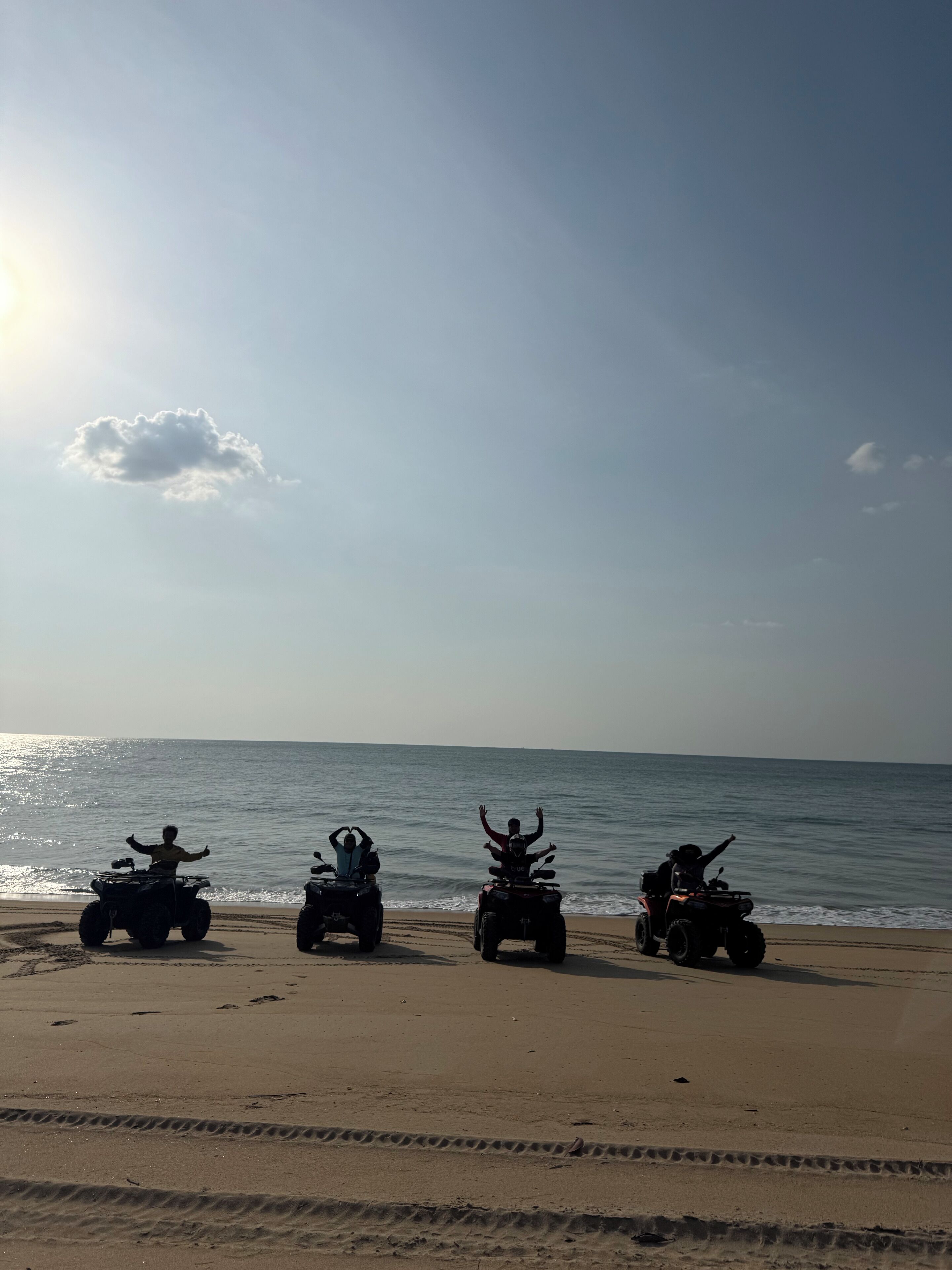 Three ATVs parked on a sandy beach with the ocean in the background.