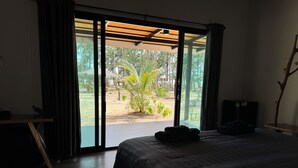 Ein Schlafzimmer mit Bett, Schreibtisch und Blick auf einen Garten durch eine Schiebetür.