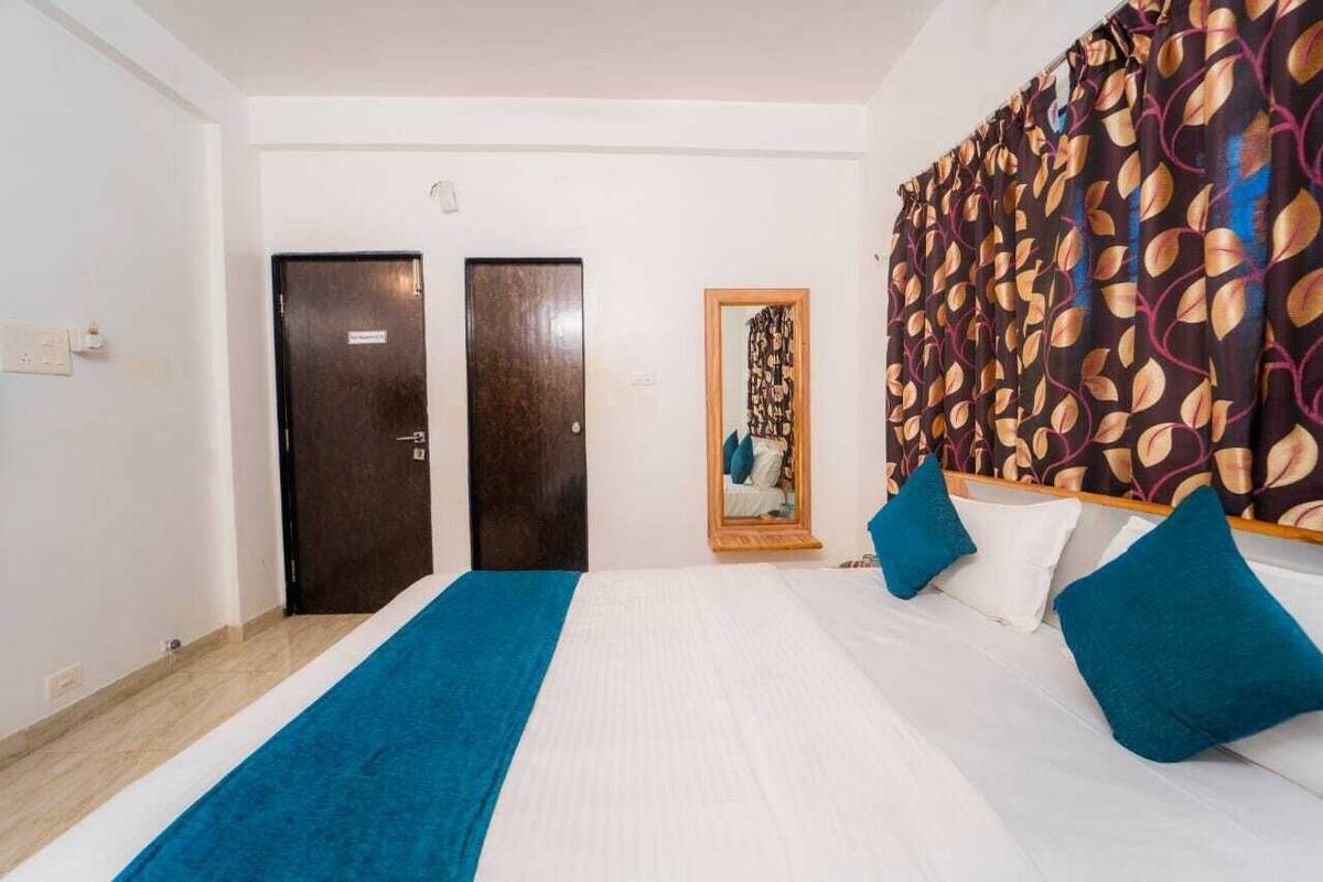 Ein Hotelzimmer mit einem Bett, zwei Türen, einem Spiegel und einem gemusterten Vorhang.