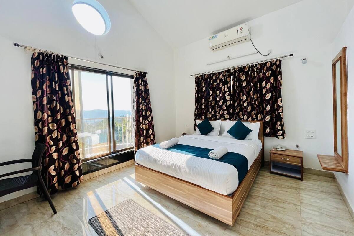 Ein Schlafzimmer mit einem großen Bett, einem Nachttisch, einem Sessel und einem Fenster mit Vorhängen.