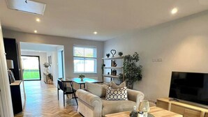 A spacious living room with a herringbone wood floor, a sofa set, a coffee table, a TV, and a bookshelf. - Newly Refurbished Bungalow- Large Garden- Parking (Ringwood)