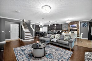 A modern living room with a grey sectional sofa, a round coffee table, and a staircase leading to the upper floor. - Resort Style - Spacious 5-BRM house in beautiful Davenport- Minutes to Disney (Davenport)