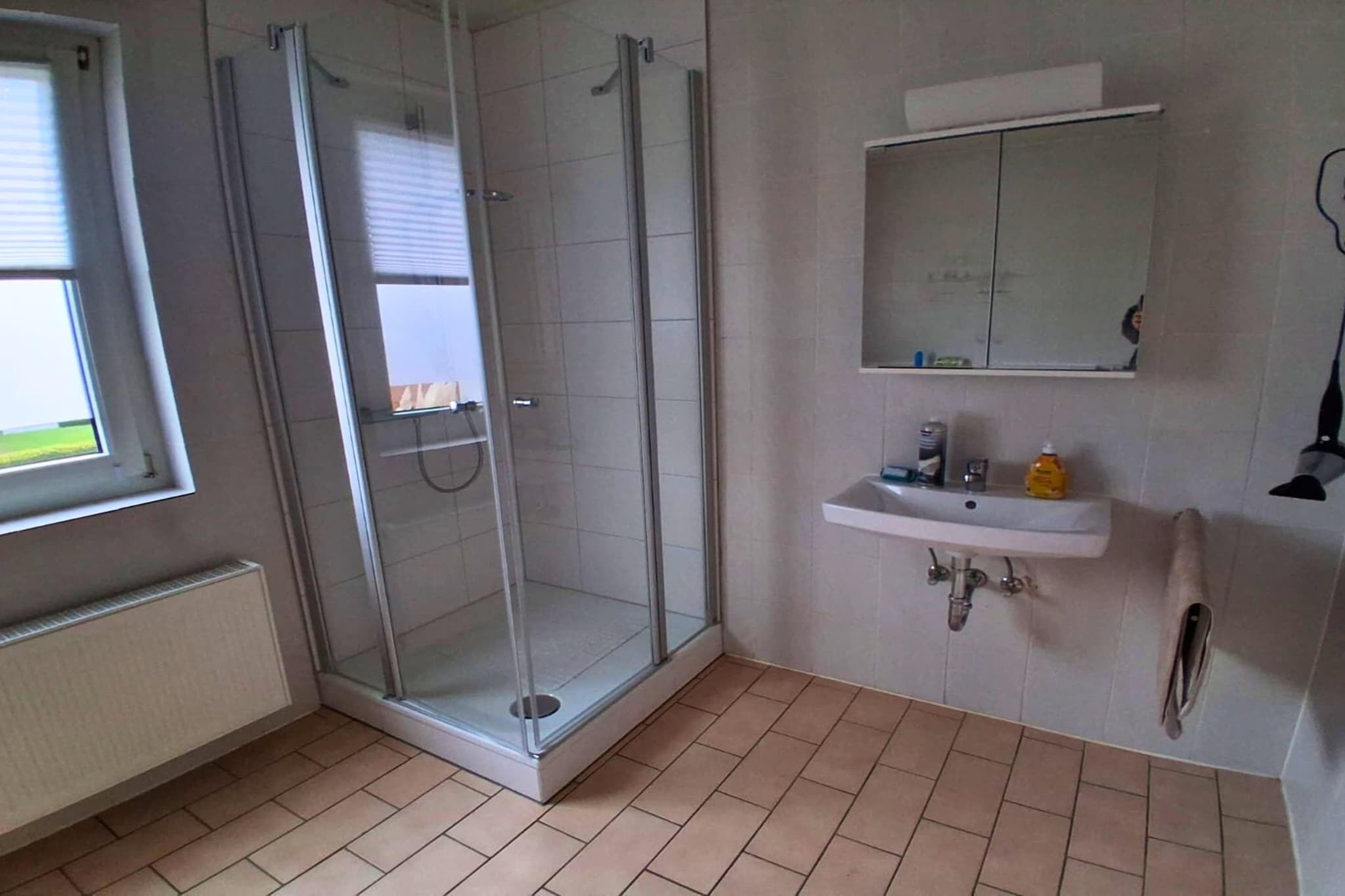 A bathroom with a glass shower enclosure, a sink with a mirror, and a window.