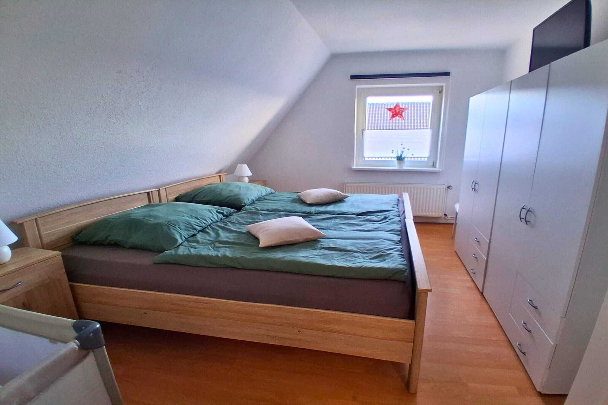 Una cama individual con ropa de cama verde, una mesita de noche con lámpara, una ventana decorada con estrellas y un armario.